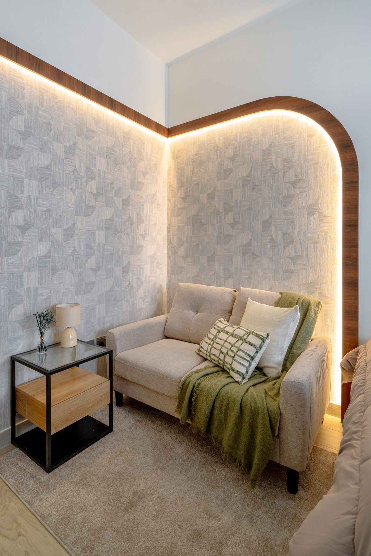 Studio apartment lounge nook with a backlit arched feature wall, loveseat and sage throw