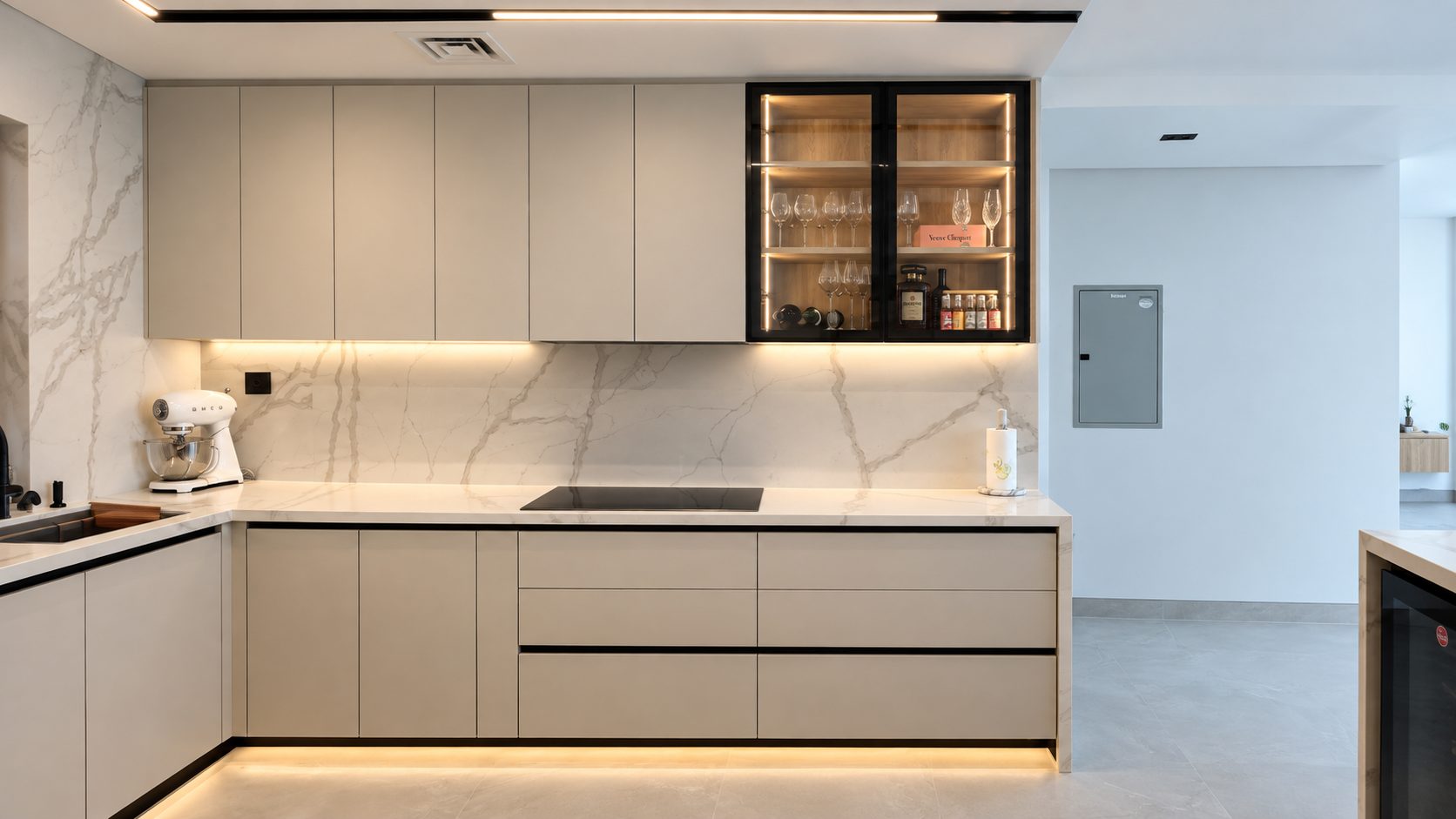 Taupe modular kitchen with marble backsplash and a lit glass-fronted display cabinet