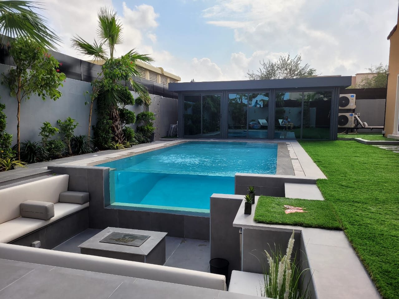 Garden with a glass-sided pool, sunken lounge seating and lawn