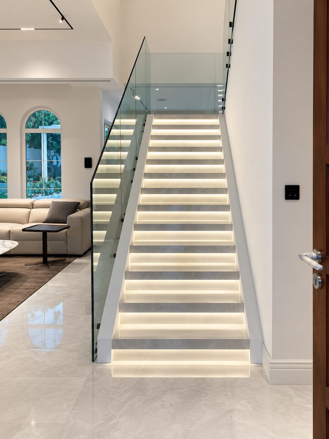 Backlit marble staircase with a frameless glass balustrade beside the living room