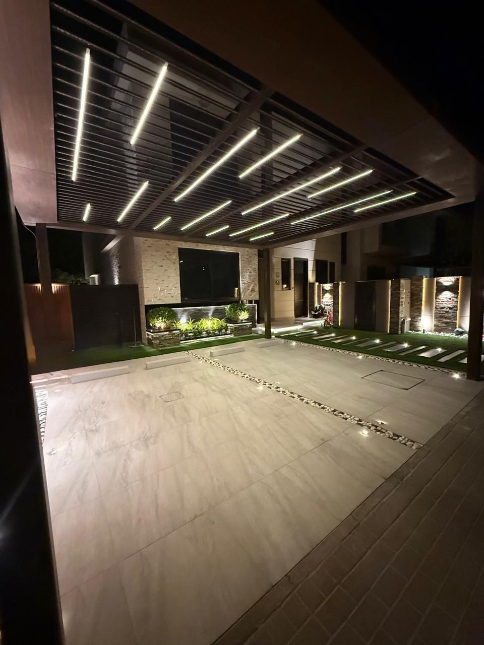 Driveway under a slatted pergola with linear LED lighting at night