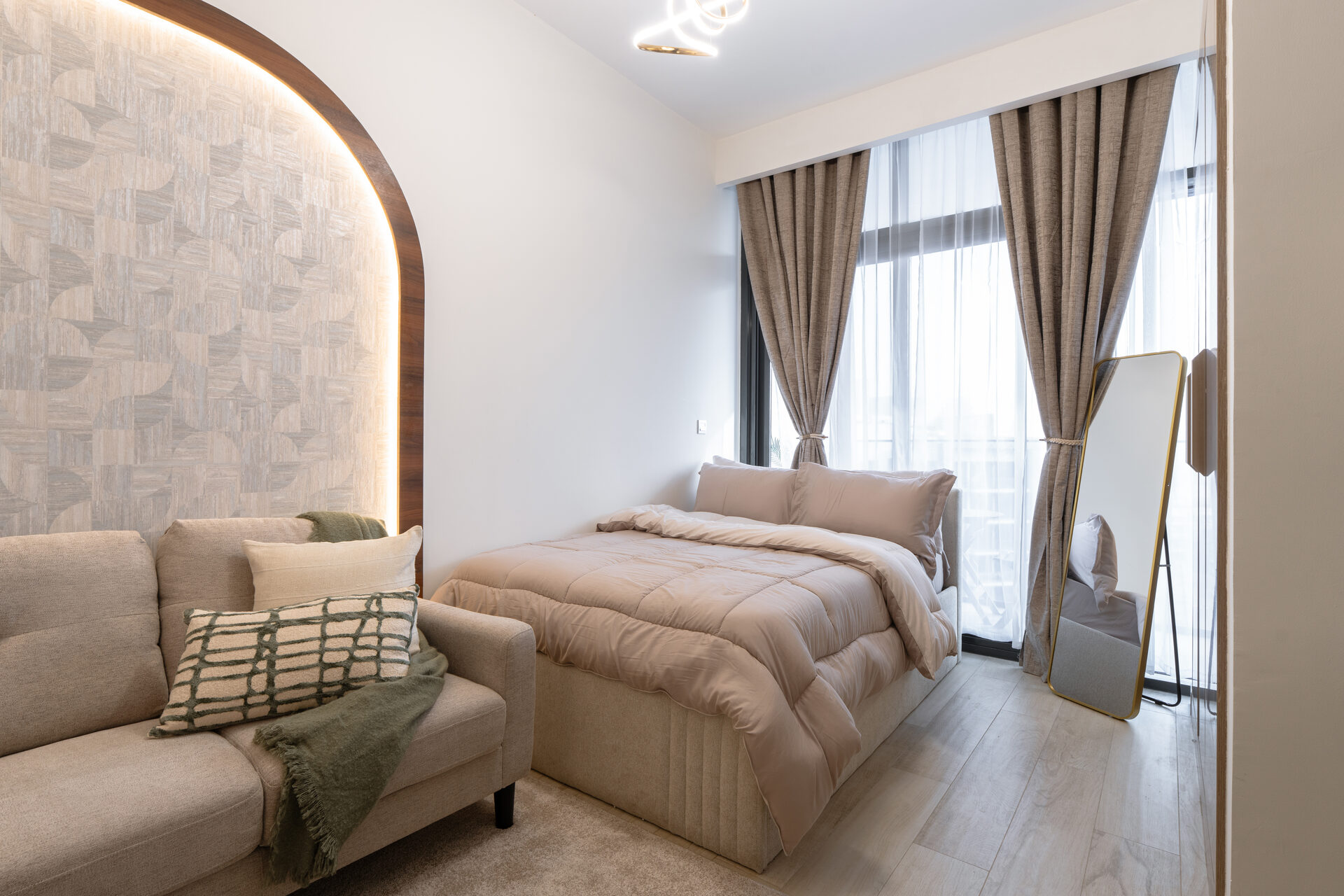 Azizi Riviera studio apartment — bed and lounge area with backlit arched feature wall